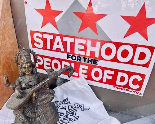 Murti of the Hindu deity Saraswati in front of a “Statehood for the People of DC” sign in a shop window 