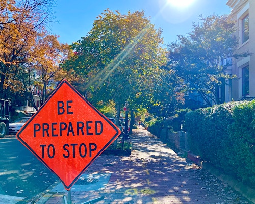 Traffic sign on neighborhood street with trees turning autumn colors, reads: “be prepared to stop”