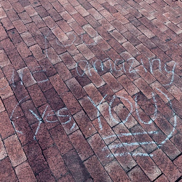 Chalk writing on neighborhood sidewalk says “you are amazing (yes YOU)”