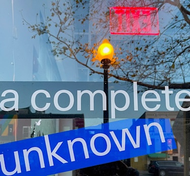 Reflection of an Exit sign in a street level window and a sign that says “a complete unknown”