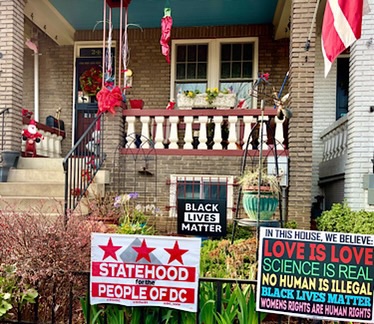 Yard signs read, “black lives matter,” “statehood for the people of DC,” and”in this house we believe that love is love, science is real, Black Lives Matter, and women’s rights are human rights.” A small Santa and a fake poinsettia decorate the porch.