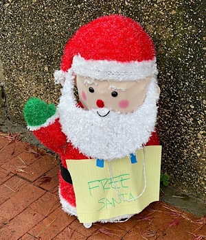 Photo of a Santa decoration with a sign around its neck that reads, “free Santa.”