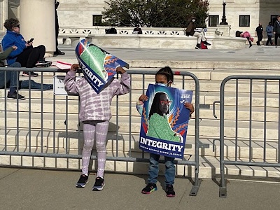 Image of two little girls holding posters with images of Justice Jackson and the word “Integrity”