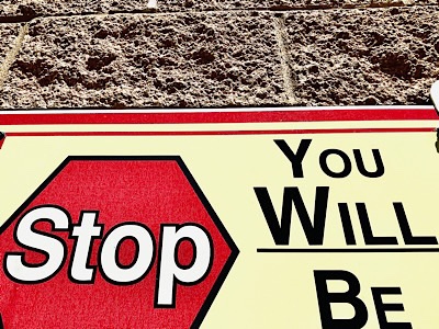 Sign on side of building shows a stop sign and the phrase “you will be “