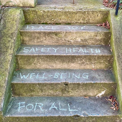 Peace Joy Safety Health Well-Being for All written on front steps in chalk