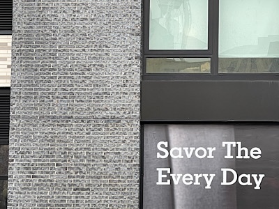 Sign on building wall reads:  “Savor the every day.”