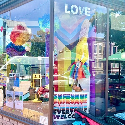 Pride signs in window display say “love” and “everyone welcome.”
