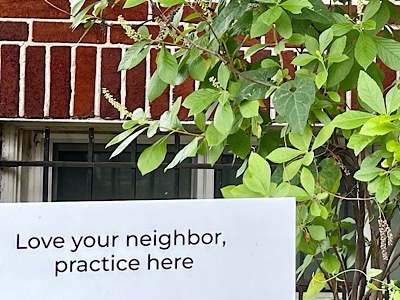 Yard sign (portion) reads:  “love your neighbor, practice here.