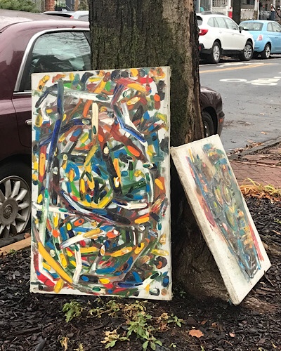 Image of two discarded paintings leaning against a tree on a city sidewalk 