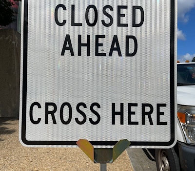 Photo of street sign that reads, “cross here, closed ahead”