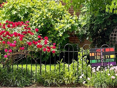 Image of red rose bush in full bloom with sign that reads, “hope, hope ,love, equality , inclusion, kindness 