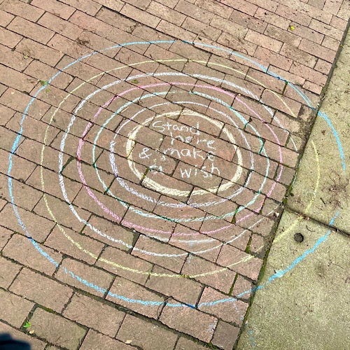 Photo of chalk drawing of concentric circles around the words, “stand here and make a wish.”