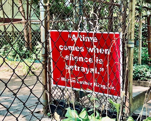 Yard sign behind chain link fence has MLK Jr quote:  “a time comes when silence is a  betrayal”