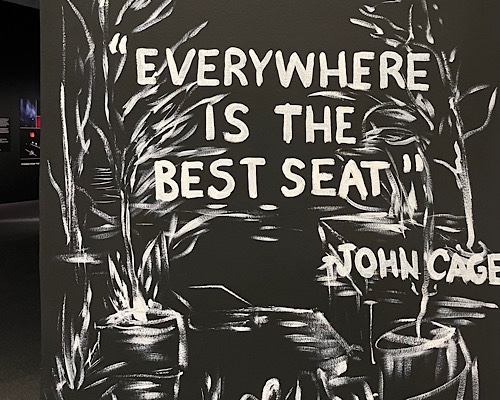 Photo of entry wall of Laurie Anderson exhibit at the Hirshhorn Museum of Art with painted words quoting John Cage:  “everywhere is the best seat.”