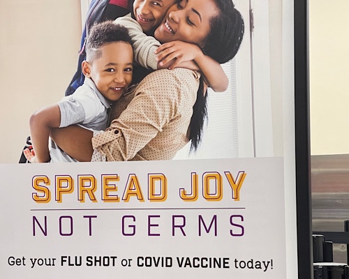 Sign showing a hugging family says, “spread joy not germs. Get your Covid-19 or flu shot today.