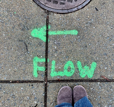 The word “flow” is painted beneath an arrow pointing left on the sidewalk 